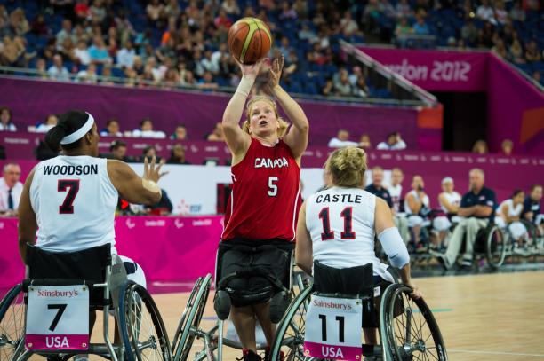 A picture of a woman in a wheelchair shooting between two defenders during a wheelchair basketball match.