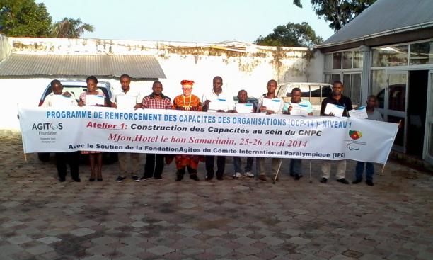 A group shot of people standing and sitting in wheelchairs behind a banner with the following text: Programme de renforcement des capacites des organisations - Niveau 1
