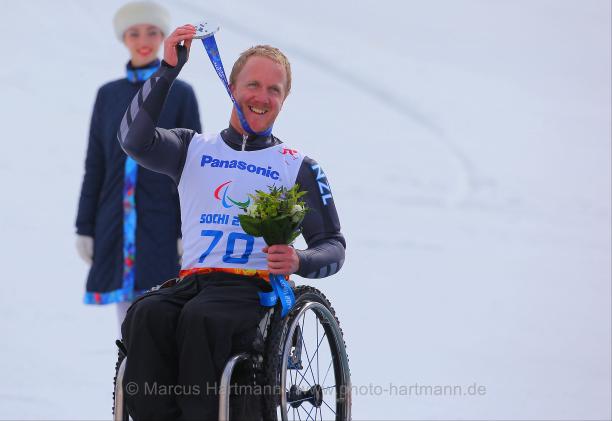 Man in wheelchair on a podium, holding his medal