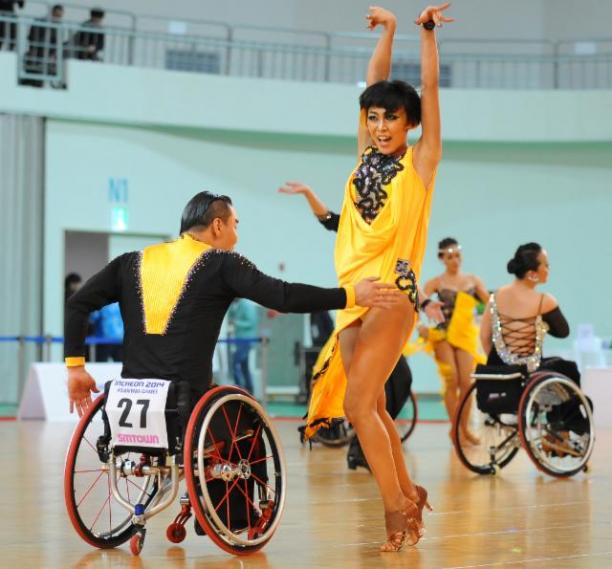 Man in wheelchair and women in dancing costumes doing an emotional latin dance move on the dance floor