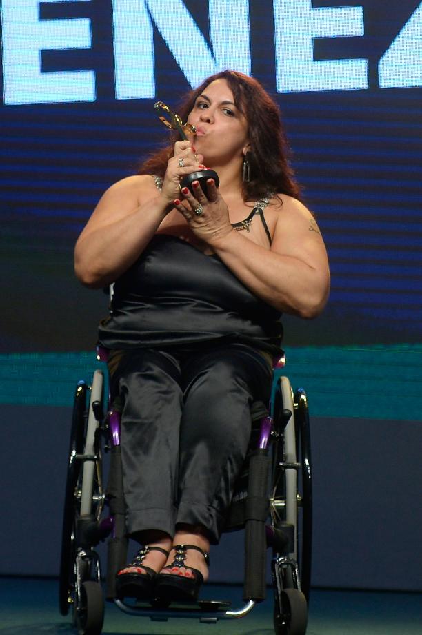 Marcia Cristina Menezes Brazil Powerlifting Women in black dress sitting in a wheelchair kissing a trophy