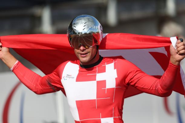 Man in red jersey with silver helmet and a Swiss flag smiling to the camera