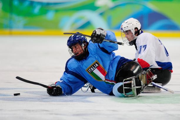 A picture of two men in sledges fighting the puck during a ice sledge hockey match