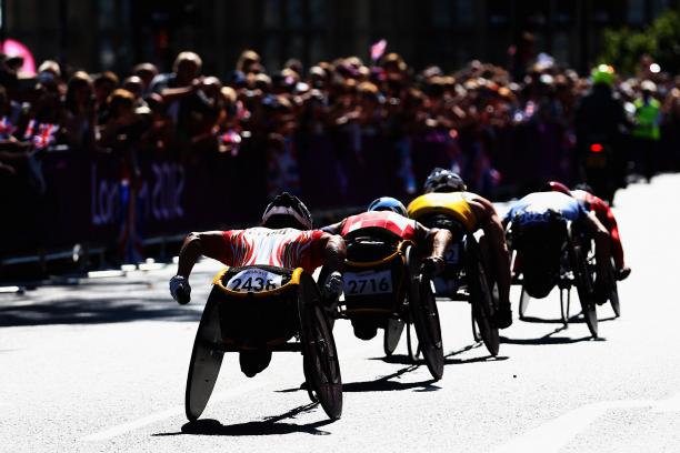 group of men in racing wheelchairs pass spectators