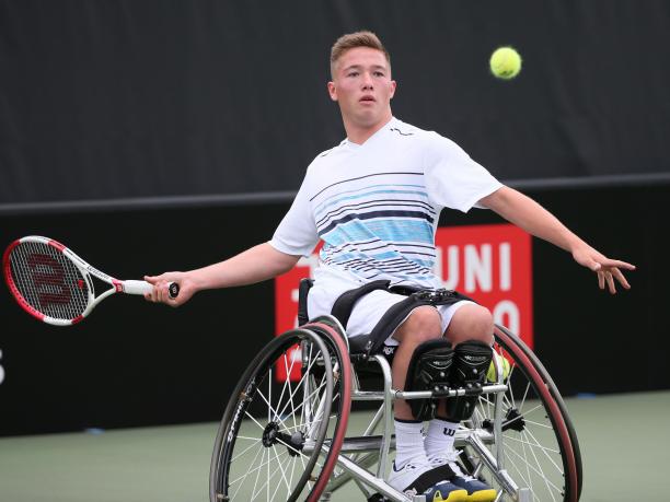 Wheelchair tennis player hits a ball back.