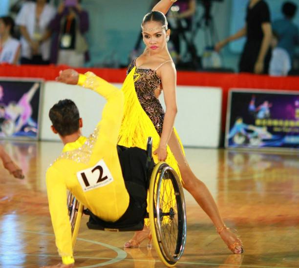 Man in wheelchair and woman standing pose while dancing