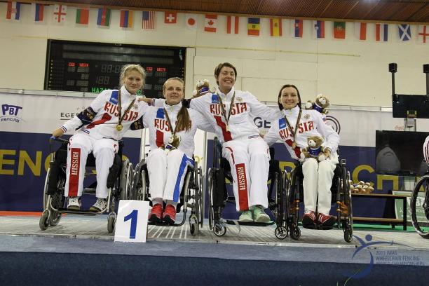 Four women in wheelchairs on a podium, posing with medals 