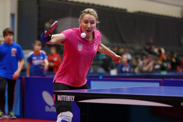 the upper body of a female playing table tennis and wearing a pink polo shirt