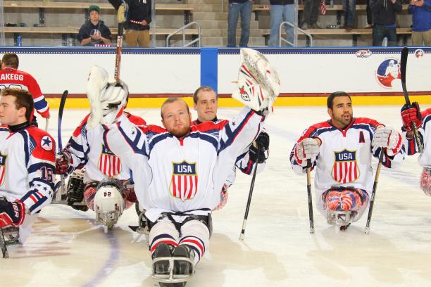 Sledge hockey players on the ice without their helmets, celebrating