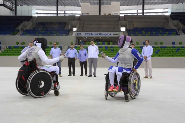 Youth Arena - Rio 2016 Two wheelchair fencers cross swords in empty arena, some people watching from behind