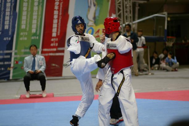 A para-taekwondo athlete does a jump kick to his opponent.