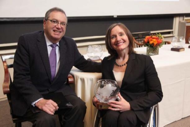 Woman in wheelchair holds trophy and poses with man.