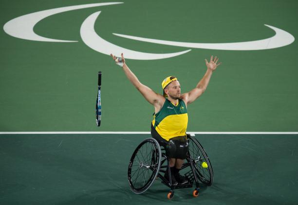 man in wheelchair throws away his tennis racket and raises his arms to celebrate