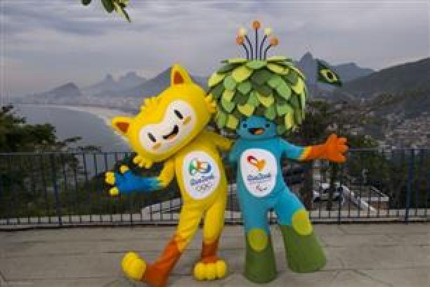 A yellow mascots and blue mascot with green leaves as hair stand on top of Rio's Sugar Loaf mountain.