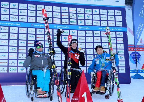 Three women in wheelchairs raising their arms with medals