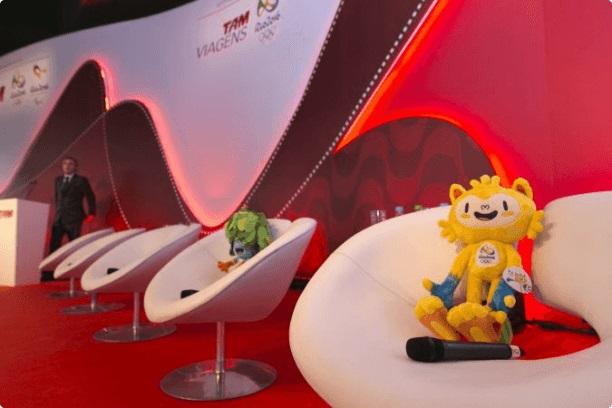 Shot of a stage with white chairs and the Rio mascots on them
