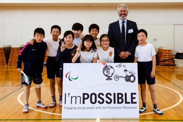 a group of children and a man smile for the camera holding a sign