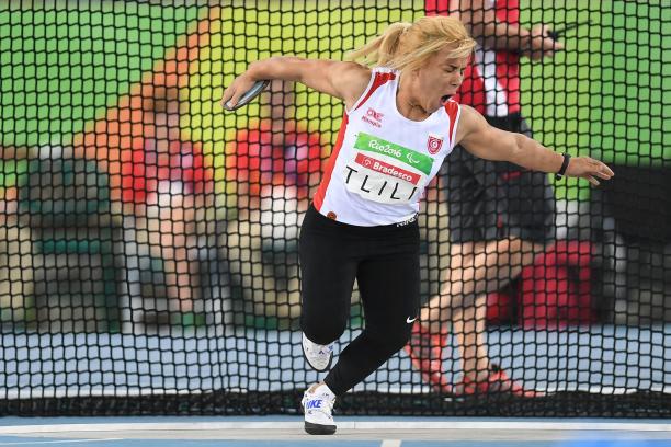 A woman in white vest and black bottoms pulls a face as she gets ready to throw a discus.