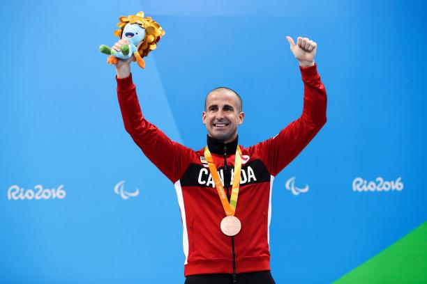 Benoit Huot a male Para swimmer raises his arms on the podium