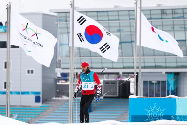 Brian McKeever - PyeongChang 2018 a male Para Nordic skier walks past the Paralympic and South Korean flags