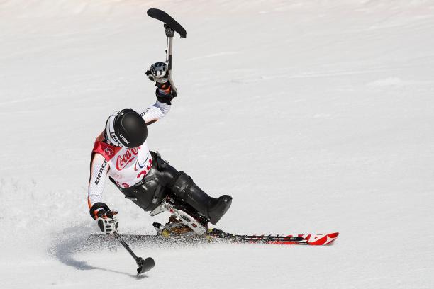 a female sit skier celebrates with her ski in the air