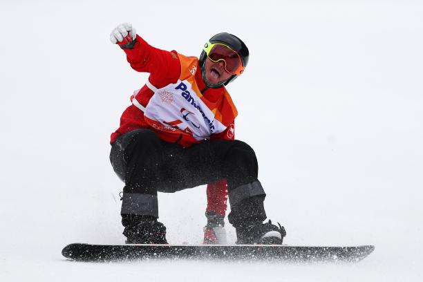 a male Para snowboarder sticks out his tongue at the end of his run