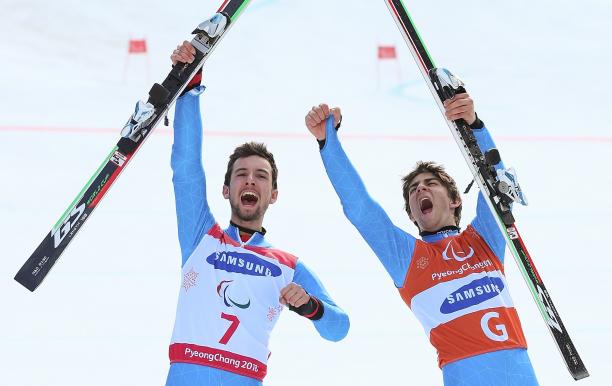 a male vision impaired skier and his guide celebrate by holding up their skis