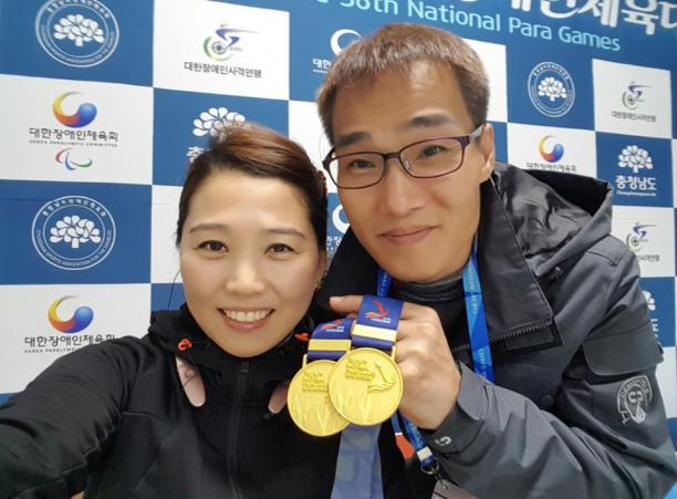 Yunri Lee a man and a woman hold up a medal
