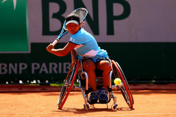 a female wheelchair tennis player plays a backhand shot