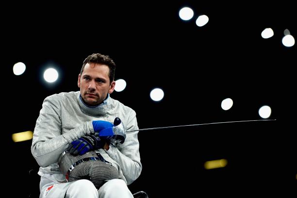 a male wheelchair fencer holding a foil and his helmet