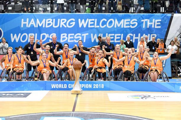 The Netherlands wheelchair basketball team A group of women in organge vests celebrate with a large trophy after winning the world title