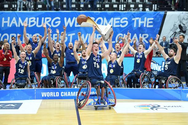 Great Britain - wheelchair basketball - Hamburg 2018 Man in wheelchair hoists basketball trophy with the men's British wheelchair basketball team behind him celerbating
