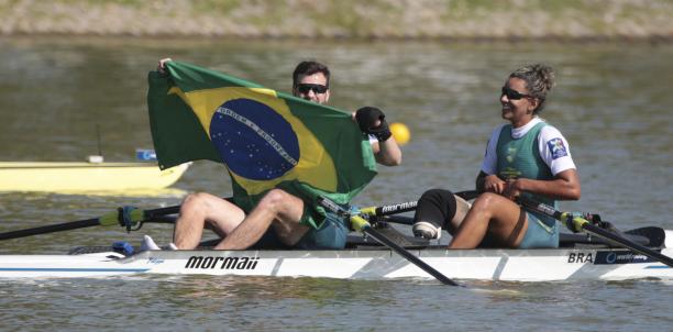 A man and woman in rowing boat celebrate, while man holds up Brazilian flag
