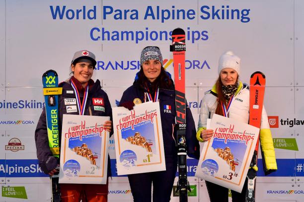 three female skiers including Marie Bochet standing on the podium holding prints