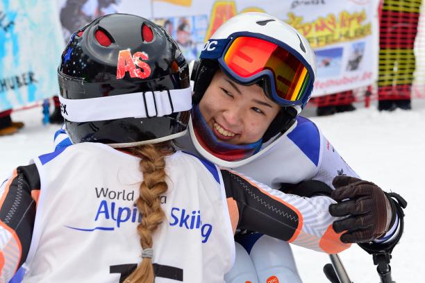 female Para alpine skier Momoka Muraoka hugs another female skier and smiles