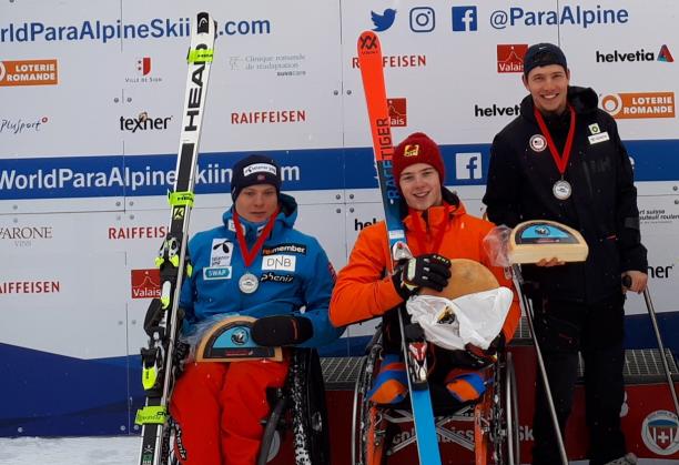 three Para alpine skiers holding up wheels of cheese on the podium
