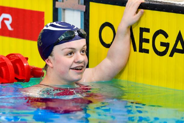 female Para swimmer Maisie Summers-Newton holds onto the wall and smiles in the pool at the end of the race