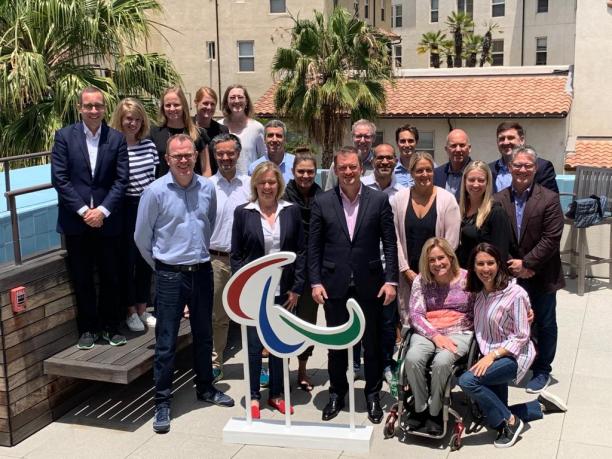 LA 2028 workshop a group of people standing in the sunshine behind an Agitos symbol