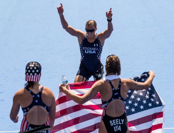 US triathletes Melissa Stockwell, Allysa Seely and Hailey Danz Two women holding the US flag waiting for their teammate to cross the finish line