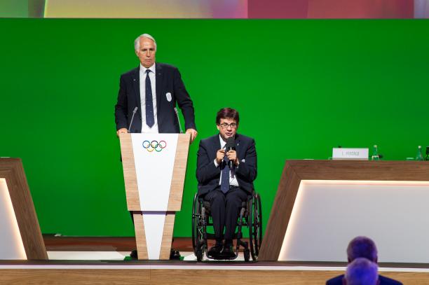 Giovanni Malago and Luca Pancalli - IOC Session 2026 Milan-Cortina A man standing and another man in a wheelchair on stage