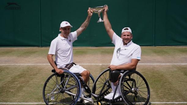 Two male wheelchair tennis players holding a trophy on a grass court