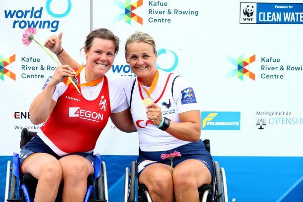 two female Para rowers in wheelchairs side hug on the podium