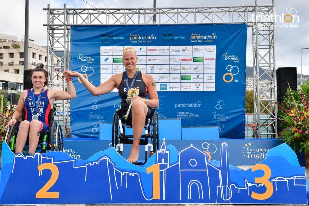 female Para triathlete Christiane Reppe holds the hand of another female athlete on the podium