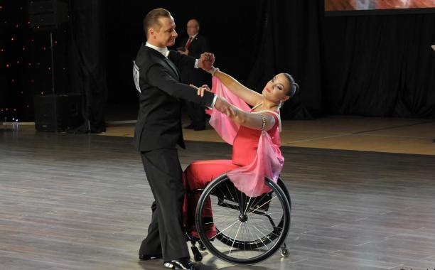 Male standing dancer dances with female partner in wheelchair