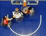 Picture taken from above the basketball basket. Three female players in wheelchairs fighting for the ball under the basket.