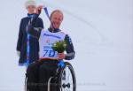 Man in wheelchair on a podium, holding his medal