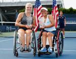 Two players sat in wheelchair holding trophies on their laps. In the background are two USA flags.