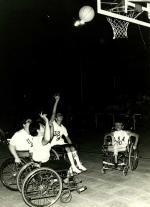 A picture of a woman in a wheelchair shooting a ball during a basketball match