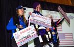 Three women on the podium, holding big checks