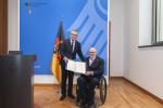 Two men, one in wheelchair and one standing in front of a German flag